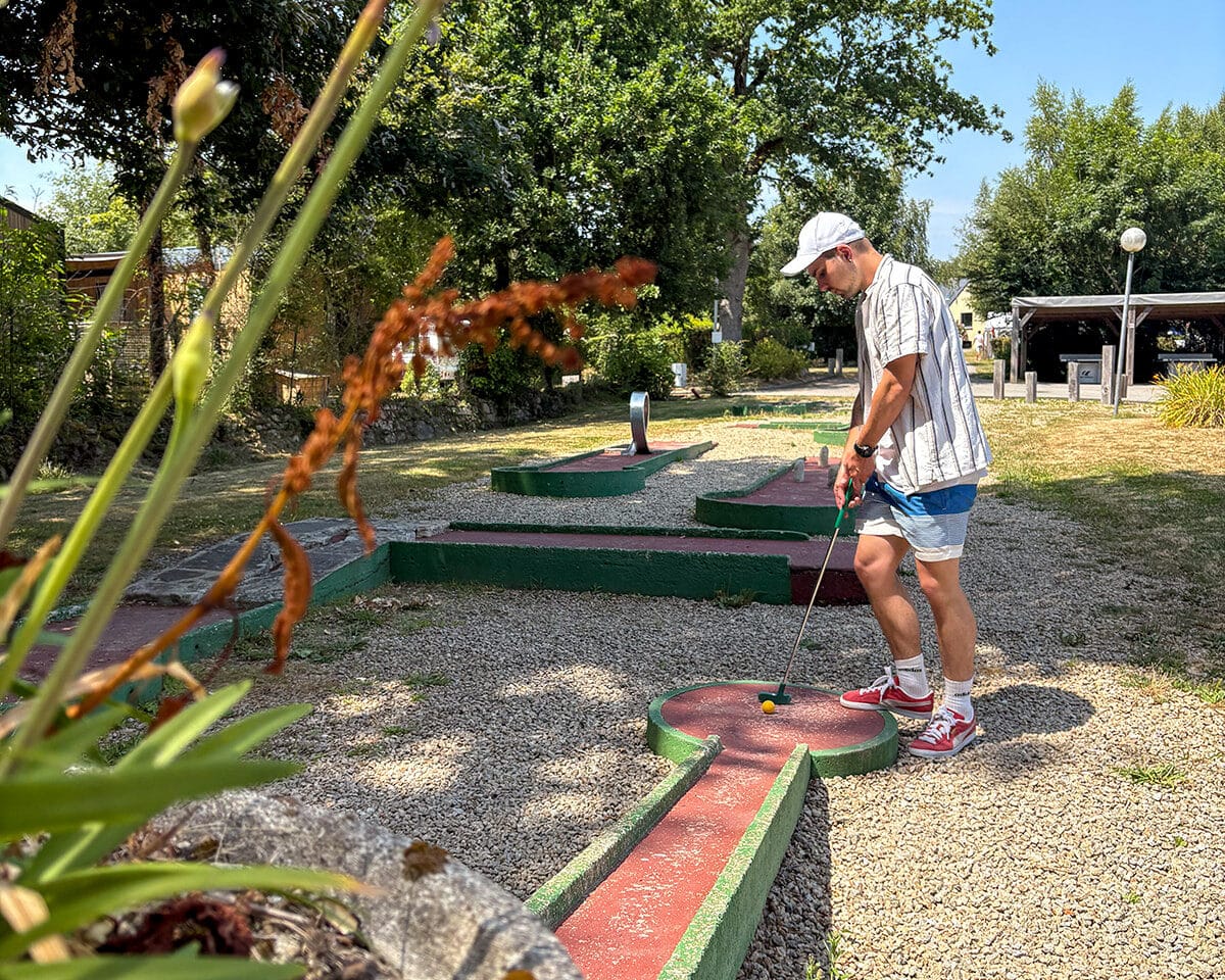 Personne jouant au mini-golf en extérieur, journée ensoleillée.